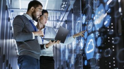 Male IT Specialist Holds Laptop and Discusses Work with Female Server Technician. They're Standing in Data Center, Rack Server Cabinet with Cloud Server Icon and Visualization
